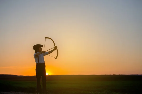 Silhouette of child playing with bow and arrows, archery shoots a bow at the target on sunset