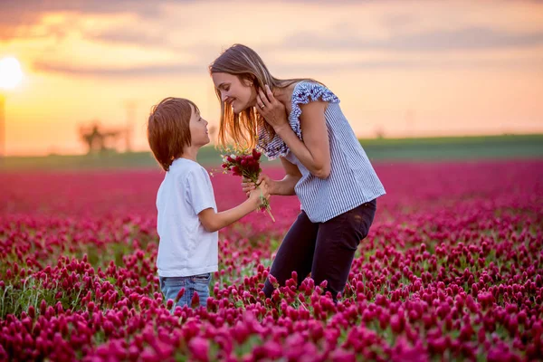Beautiful kid and mom in spring park, flower and present. Mothers day celebration concept. Mom and son in crimson clover field, mom getting bouquet of wild flowers gathered from her child for Mothers day