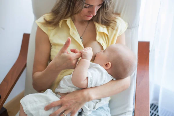 居心地の良い日当たりの良いベッドルームの肘掛け椅子に座っている彼女の男の子の Brestfeeding を保持している若い母親 — ストック写真