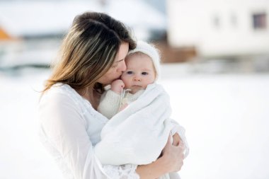 Beyaz elbiseli güzel bir anne ve örgü tulumlu şirin bir çocuk güneşli bir kış gününde güzel kış portrelerini çektiler.