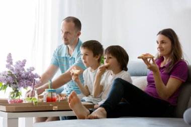 Beautiful young family with children, eating pizza at home and watching TV on a sunday clipart