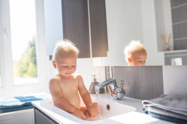 Bebek alarak banyo lavabo. Köpük ve sabun köpüğü ile pencere güneşli banyoda ile oynayan çocuk. Küçük çocuk banyo. Su eğlenceli çocuklar için. Hijyen ve cilt bakımı çocuk için. Banyo odası iç