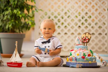 Küçük yürümeye başlayan çocuk, giyinmiş olarak denizci, deniz Tema kek, tekne, balıklar ve aqua hayvanlar, yeşil backgground ile ilk Doğum günü kutluyor