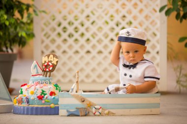 Küçük yürümeye başlayan çocuk, giyinmiş olarak denizci, deniz Tema kek, tekne, balıklar ve aqua hayvanlar, yeşil backgground ile ilk Doğum günü kutluyor