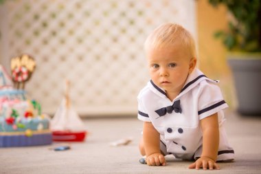 Küçük yürümeye başlayan çocuk, giyinmiş olarak denizci, deniz Tema kek, tekne, balıklar ve aqua hayvanlar, yeşil backgground ile ilk Doğum günü kutluyor
