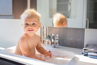 Bebek alarak banyo lavabo. Köpük ve sabun köpüğü ile pencere güneşli banyoda ile oynayan çocuk. Küçük çocuk banyo. Su eğlenceli çocuklar için. Hijyen ve cilt bakımı çocuk için. Banyo odası iç