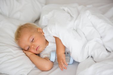 Tatlı küçük oğlan, mama sütüyle şişeyle uyuyor. Bebek karyolasında yorgun bir çocuk