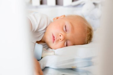 Tatlı küçük oğlan, mama sütüyle şişeyle uyuyor. Bebek karyolasında yorgun bir çocuk