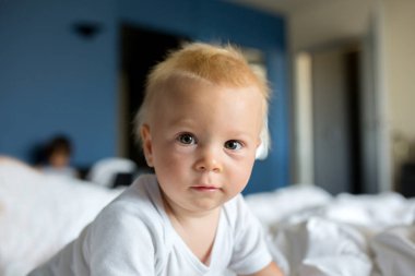 Güneşli otel odasında yatakta oynayan erkek bebek