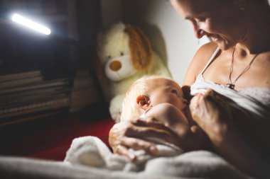 Genç güzel annem, emzirme gece, onun yeni doğan bebek çocuk loş ışık. Anne emzirme bebek