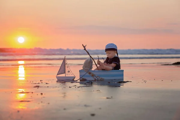 可爱的孩子 甜美的男孩 玩小船 泰迪熊和鱼在日落的海洋边缘 美丽的日落 — 图库照片