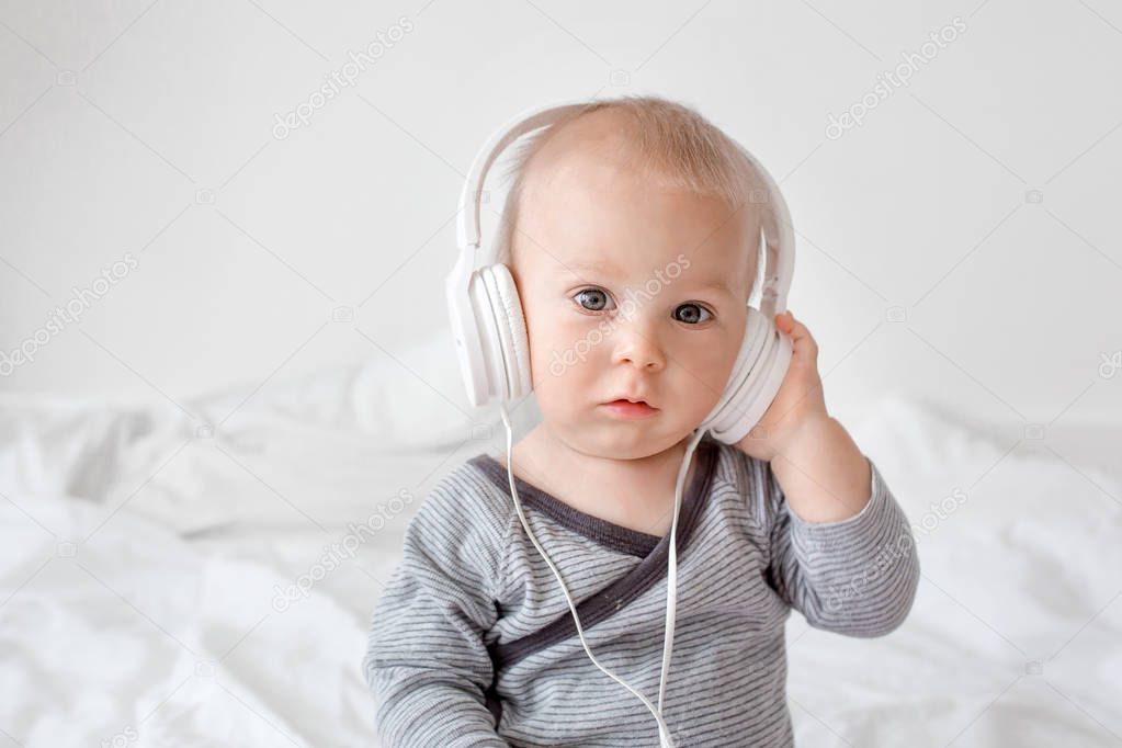 Cute little toddler baby boy listening music with head phones in bed