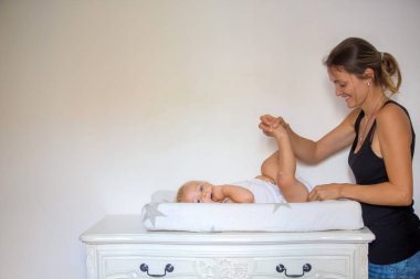 Mutlu anne ile bebek bezini değiştirirken oynarken. Gülümseyen genç kadın bebek oğluyla evde tablo değiştirme. Birlikte oynayan neşeli anne ve yürümeye başlayan çocuk yakın çekim.