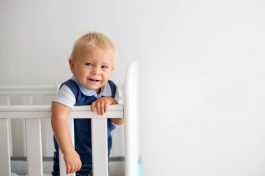 Parmaklıkların arasından seyir Bebek karyolası mutsuz hissediyor güzel giyinmiş, üzgün küçük oğlu,