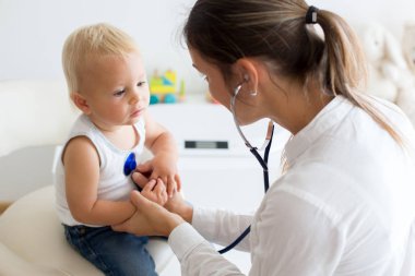 Çocuk doktoru, bebeğini muayene ediyor. Doktor steteskop kullanarak çocuğu dinliyor ve kalp atışlarını kontrol ediyor.