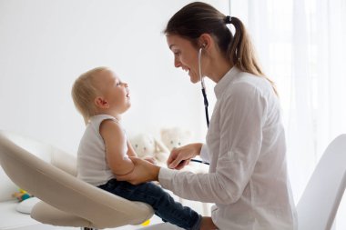 Çocuk doktoru, bebeğini muayene ediyor. Doktor steteskop kullanarak çocuğu dinliyor ve kalp atışlarını kontrol ediyor.