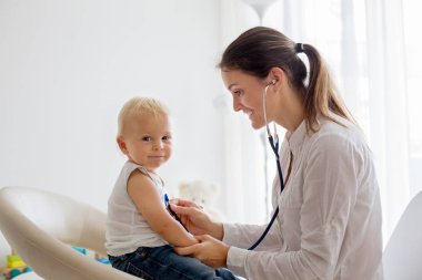 Çocuk doktoru, bebeğini muayene ediyor. Doktor steteskop kullanarak çocuğu dinliyor ve kalp atışlarını kontrol ediyor.