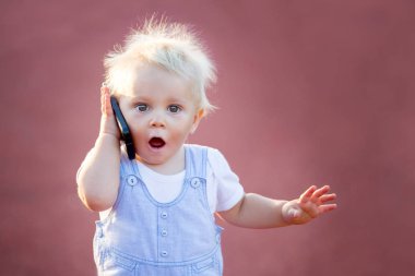 Parkta cep telefonuyla oynayan sevimli bir oğlan çocuğu, dijital teknolojiler bir çocuğun elinde. Akıllı telefonlu bir bebeğin portresi