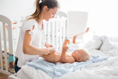 Genç anne, güneşli yatak odasında bebek bezi değiştiriyor.