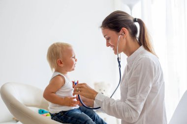 Çocuk doktoru, bebeğini muayene ediyor. Doktor steteskop kullanarak çocuğu dinliyor ve kalp atışlarını kontrol ediyor.