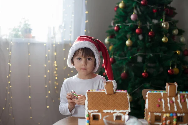 かわいい男の子 ジンジャーブレッド クッキーの家を作る家庭でクリスマス ツリーの前で子遊んで 楽しんで クリスマス コンセプトを飾る — ストック写真