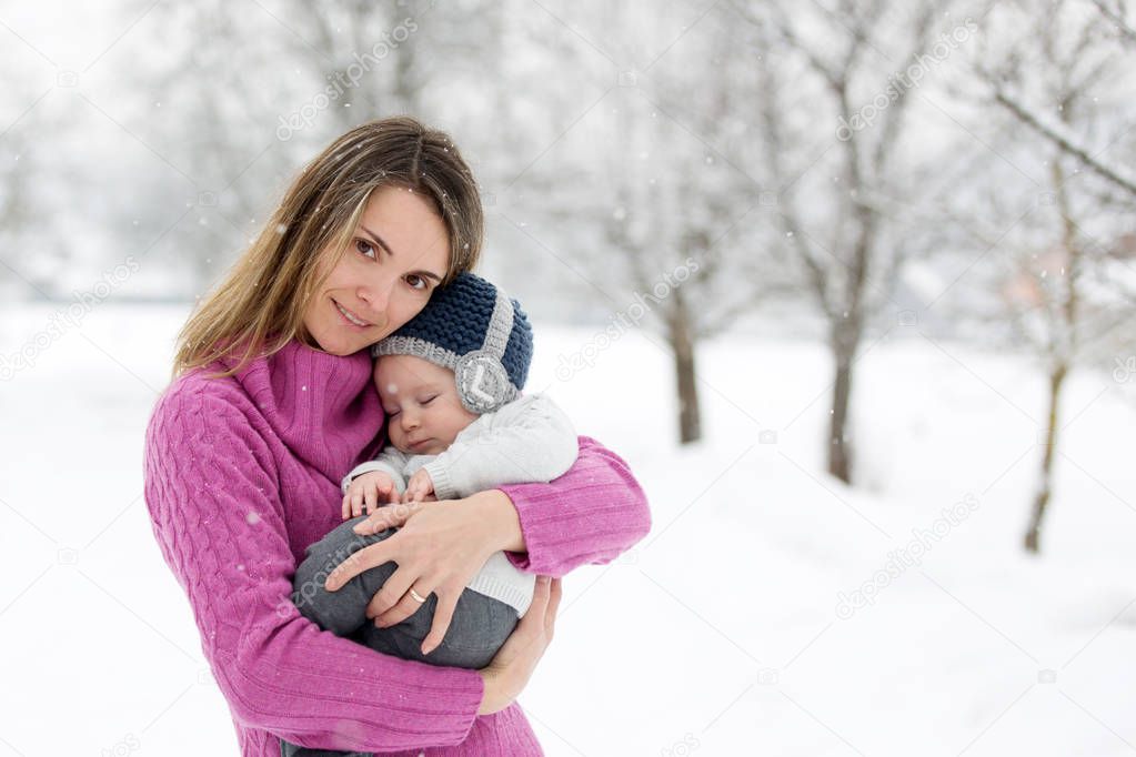 Beautiful mother and cute baby boy in knitted sweater, having taken their beautiful winter outdoor portrait on a sunny winter snowy day