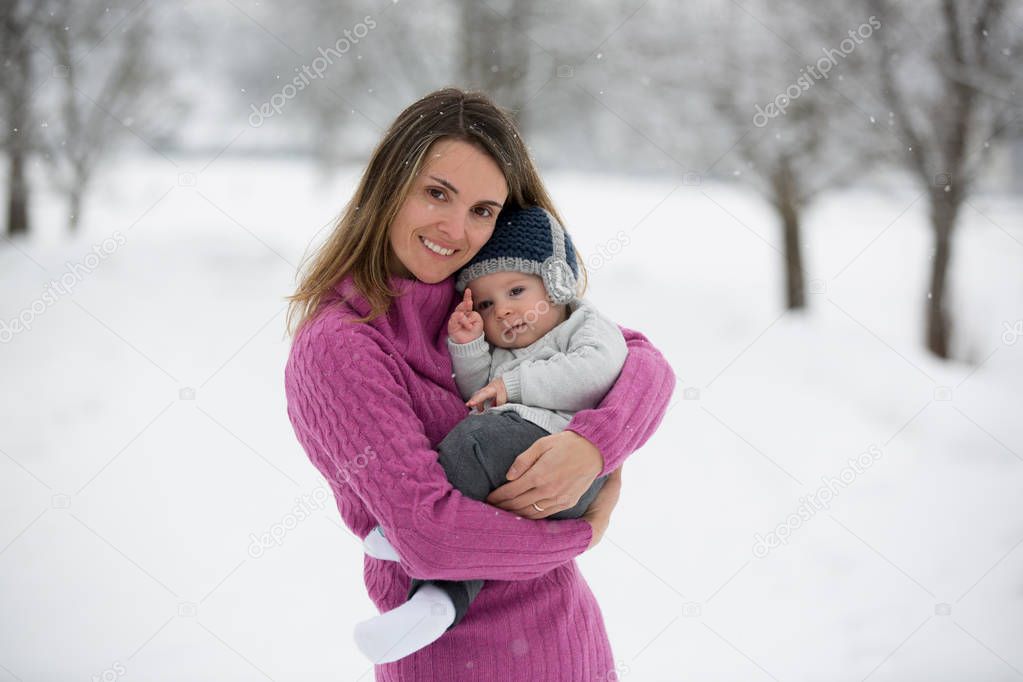 Beautiful mother and cute baby boy in knitted sweater, having taken their beautiful winter outdoor portrait on a sunny winter snowy day