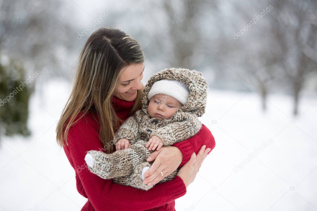 Beautiful mother and cute baby boy in knitted onesie, having taken their beautiful winter outdoor portrait on a sunny winter snowy day