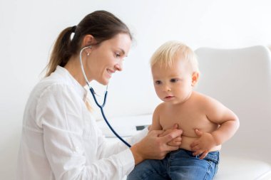 Çocuk doktoru, bebeğini muayene ediyor. Doktor steteskop kullanarak çocuğu dinliyor ve kalp atışlarını kontrol ediyor.