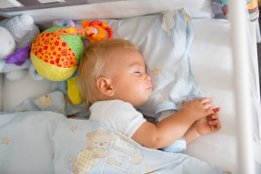 Tatlı küçük oğlan, mama sütüyle şişeyle uyuyor. Bebek karyolasında yorgun bir çocuk