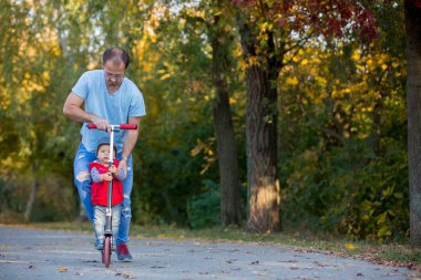 Babası onun bir sonbahar parkta yürümeye başlayan çocuk evlat scooter sürme. . Etkin aile boş. Spor, boş zaman çocuklar konsepti ile.