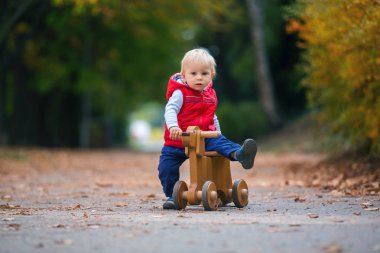 Oyuncak ayı, olan küçük yürümeye başlayan çocuk ahşap köpek denge Sonbahar Park sıcak güneşli bir gün, çocuk eğlence aktiviteleri ve mutluluk kavramı üzerinde bisiklete binmek