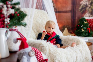Noel ağacı ve arka planda oda ışıkları ile sallanan sandalyede oturup, uyku, kurabiye yemek Noel Baba bornoz giymiş erkek bebek, sevimli çocuk. Mutlu Noeller. Tatil sezonu.