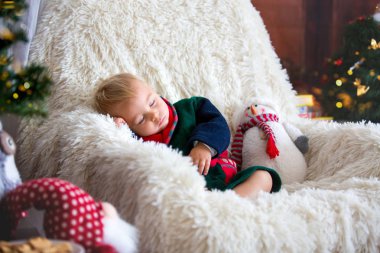 Noel ağacı ve arka planda oda ışıkları ile sallanan sandalyede oturup, uyku, kurabiye yemek Noel Baba bornoz giymiş erkek bebek, sevimli çocuk. Mutlu Noeller. Tatil sezonu.