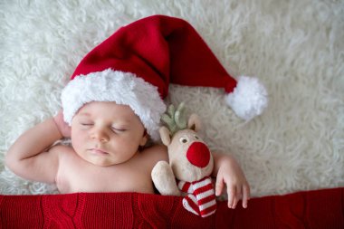 Little sleeping newborn baby boy, wearing Santa hat and pants, holding toy clipart