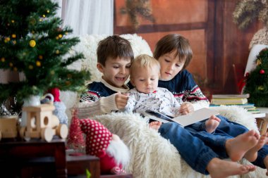 Üç çocuk, erkek kardeşler, kitap okumak sallanan sandalye ile Noel dekorasyonu, rahat oturma odasında otururken gülümseyen