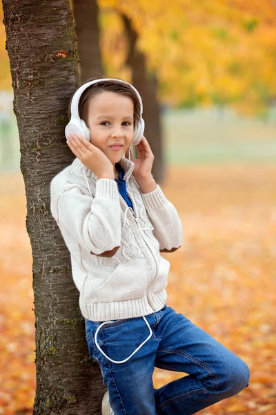 未就学児 ヘッドフォンや夕日秋の公園で携帯電話で音楽を聴くの甘い肖像画 — ストック写真