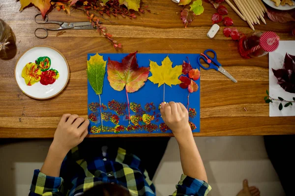 Children, applying leaves using glue, scissors, and paint, while doing arts and crafts in school, autumntime