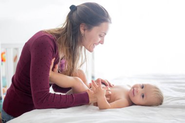 Genç anne, güneşli yatak odasında bebek bezi değiştiriyor.