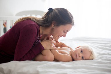 Genç anne, güneşli yatak odasında bebek bezi değiştiriyor.