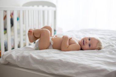 Genç anne, güneşli yatak odasında bebek bezi değiştiriyor.