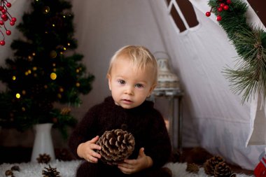 Sevimli bebek bebek çocuk teepee içinde oynarken el yapımı örgü ayı kostümlü Noel, kahverengi zemin üzerinde atış stüdyo dekore edilmiş