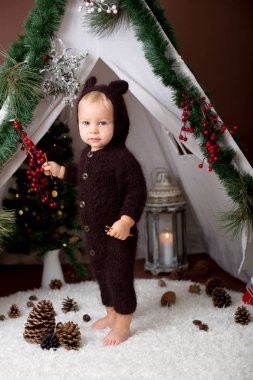Sevimli bebek bebek çocuk teepee içinde oynarken el yapımı örgü ayı kostümlü Noel, kahverengi zemin üzerinde atış stüdyo dekore edilmiş
