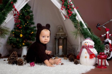 Sevimli bebek bebek çocuk teepee içinde oynarken el yapımı örgü ayı kostümlü Noel, kahverengi zemin üzerinde atış stüdyo dekore edilmiş