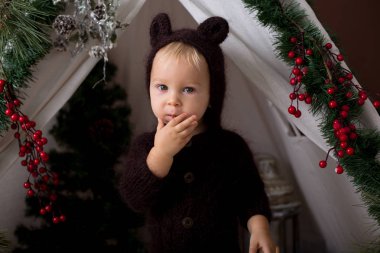 Sevimli bebek bebek çocuk teepee içinde oynarken el yapımı örgü ayı kostümlü Noel, kahverengi zemin üzerinde atış stüdyo dekore edilmiş