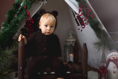 Sevimli bebek bebek çocuk teepee içinde oynarken el yapımı örgü ayı kostümlü Noel, kahverengi zemin üzerinde atış stüdyo dekore edilmiş