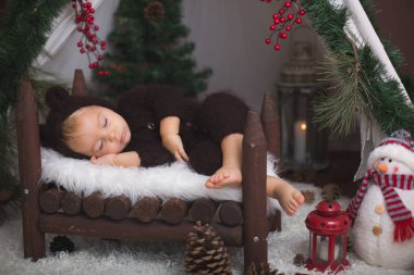 Ahşap teepee yatakta uyuyan sevimli bebek bebek çocuk el yapımı örgü ayı kostümlü, Noel için dekore edilmiştir.