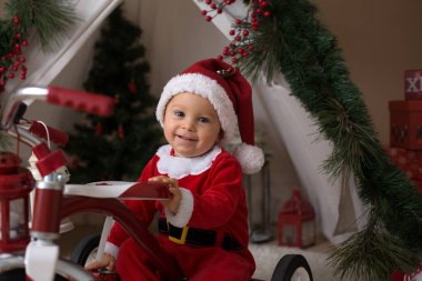 Sevimli küçük yürümeye başlayan çocuk için Noel Baba kostüm, evde teepee önünde oynarken dekore canta giymiş erkek bebek
