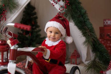 Sevimli küçük yürümeye başlayan çocuk için Noel Baba kostüm, evde teepee önünde oynarken dekore canta giymiş erkek bebek