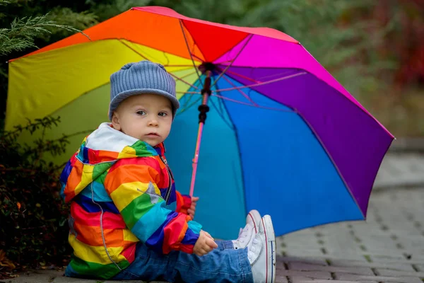 Rainboy コートと野外で遊ぶ雨の後水たまり Iand のジャンプ色とりどりの傘と甘い面白い子 — ストック写真